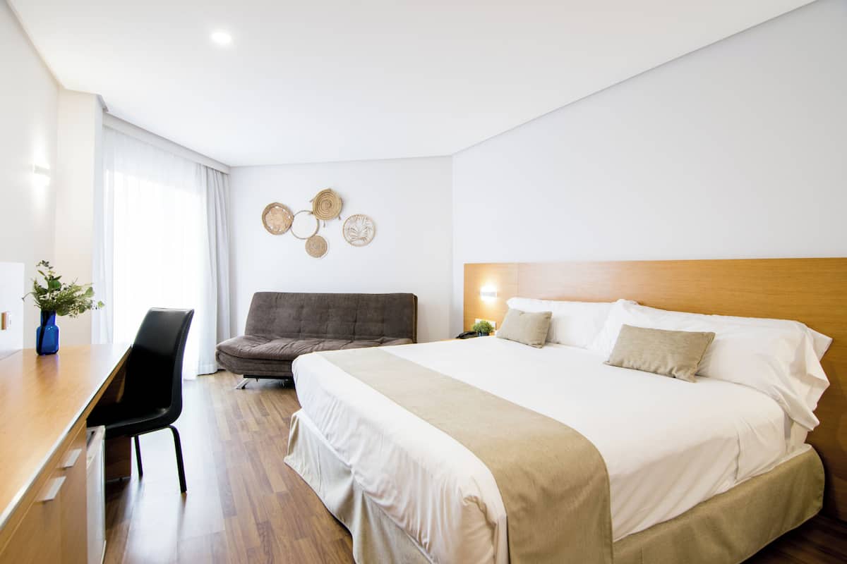 A hotel room with a bed, a desk, a chair, and a wall with decorative plates.