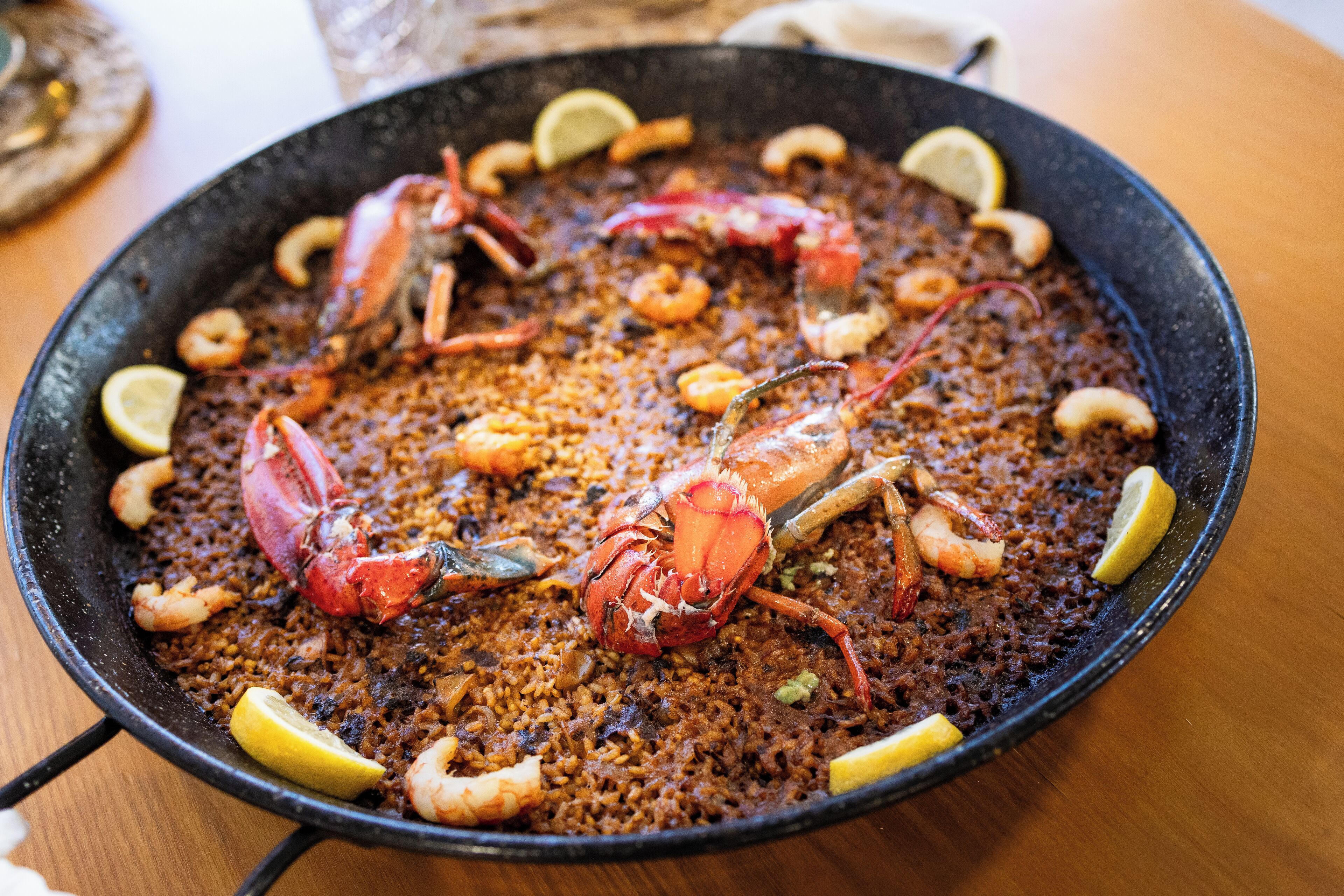 A large black pan filled with seafood paella, garnished with lemon slices and shrimp.