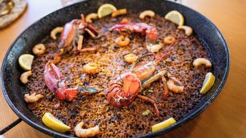 A large black pan filled with seafood paella, garnished with lemon slices and shrimp.