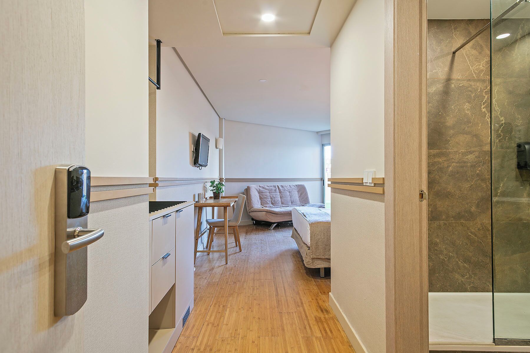A compact room with a kitchenette, a bed, a small table, and a glass shower.
