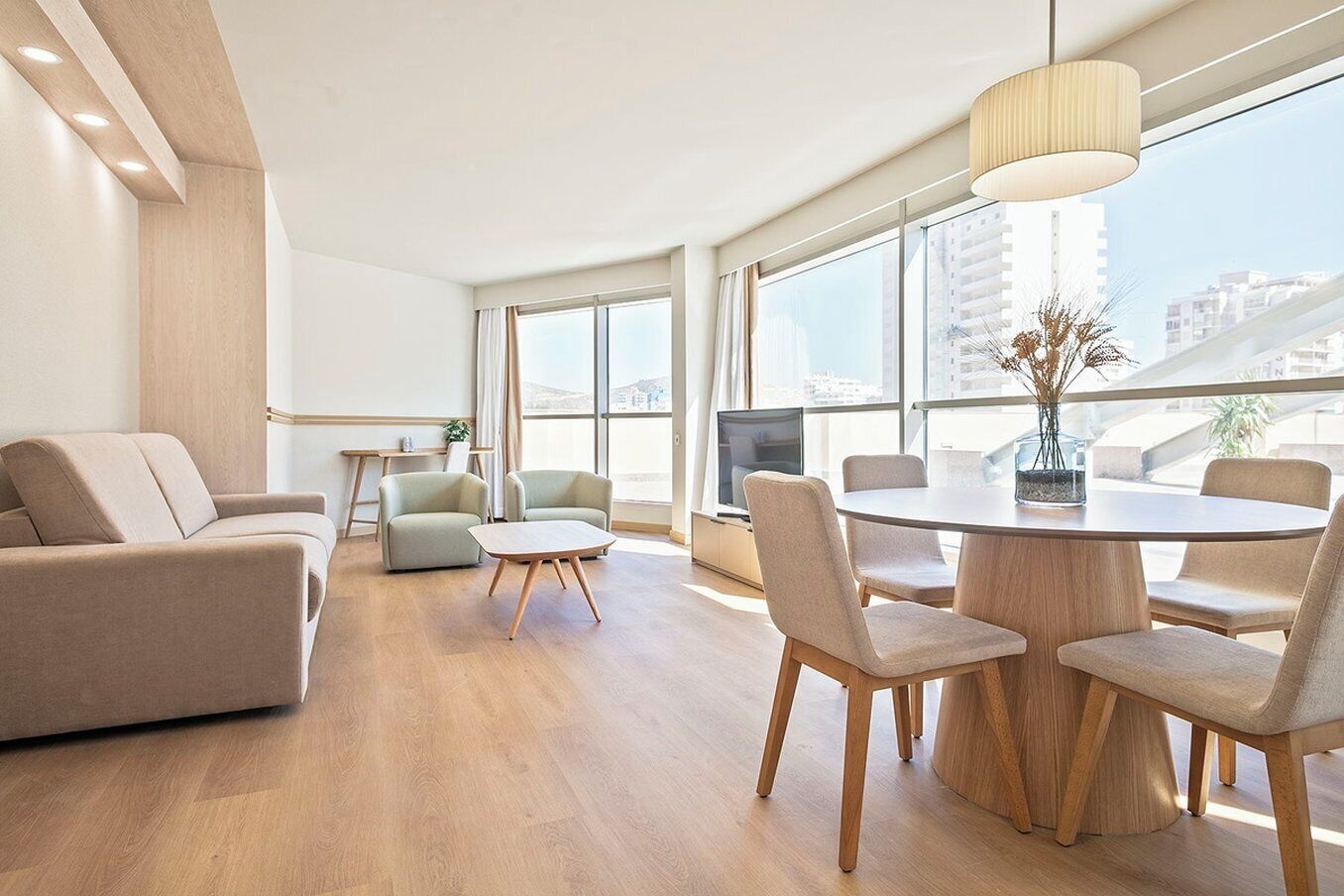 Ein modernes Hotelzimmer mit großem Fenster, einem runden Esstisch und einer Couch.