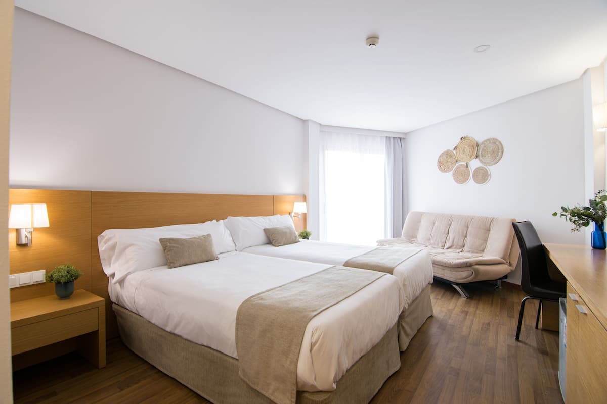 Habitación de hotel con dos camas, un escritorio, una silla, una lámpara y un adorno en la pared.