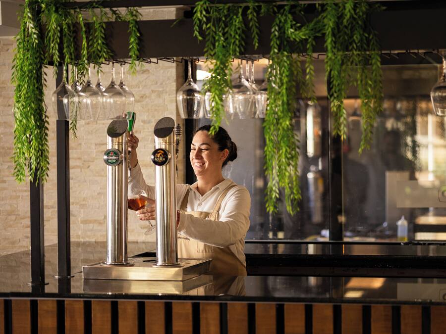 A bar area with a bartender serving drinks, a beer tap, and hanging glassware.