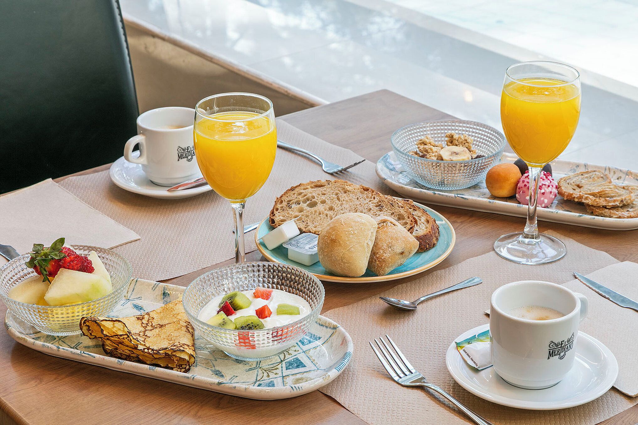 Una escena de desayuno con diversos alimentos, un vaso de jugo de naranja y una taza de café sobre una mesa.