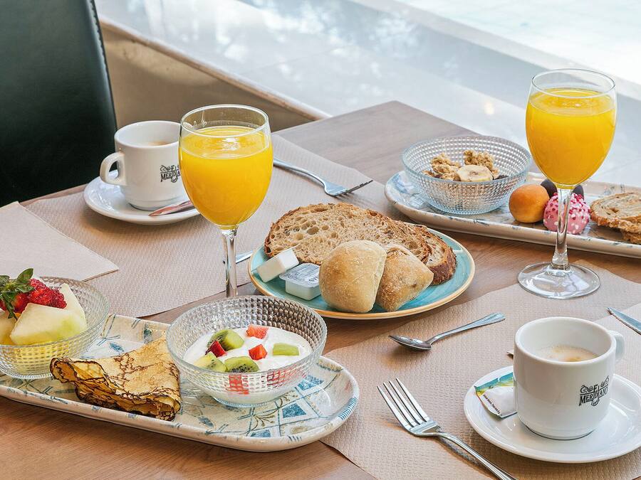 Una escena de desayuno con diversos alimentos, un vaso de jugo de naranja y una taza de café sobre una mesa.