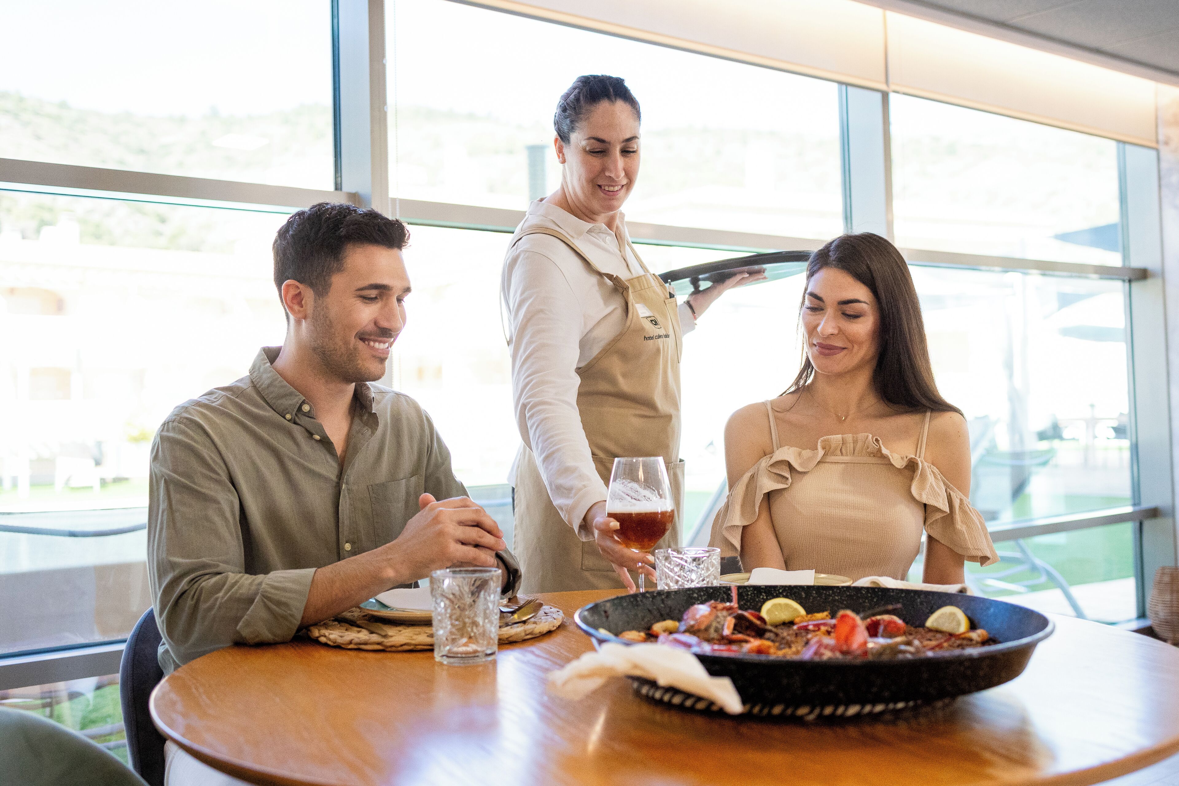 A dining table with a meal, a waiter, and a guest.