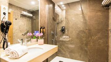 Un baño moderno con ducha envuelta en vidrio, tocador con espejo y secador de pelo en la pared.