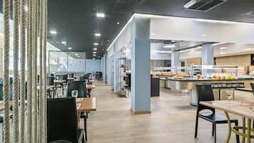 Un comedor moderno con varias mesas y sillas, un mostrador de buffet y una zona de cocina.