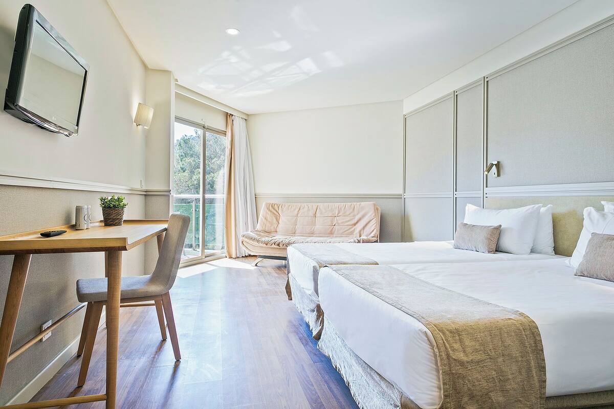 Habitación de hotel con cama, escritorio, silla, ventana grande y televisor montado en la pared.