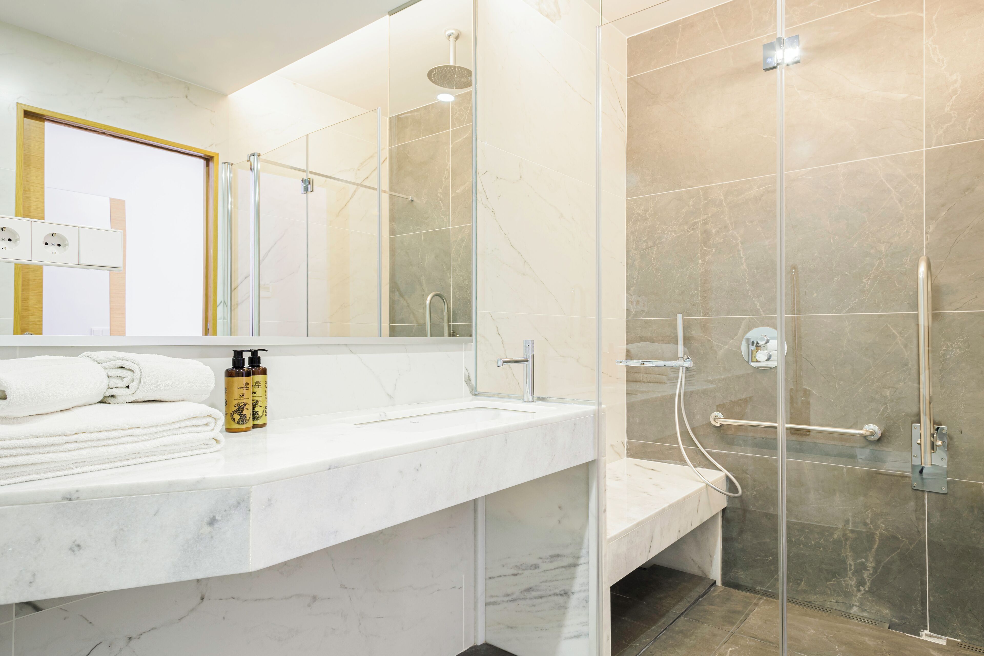 A modern bathroom with a marble countertop, a glass shower enclosure, and a bench.
