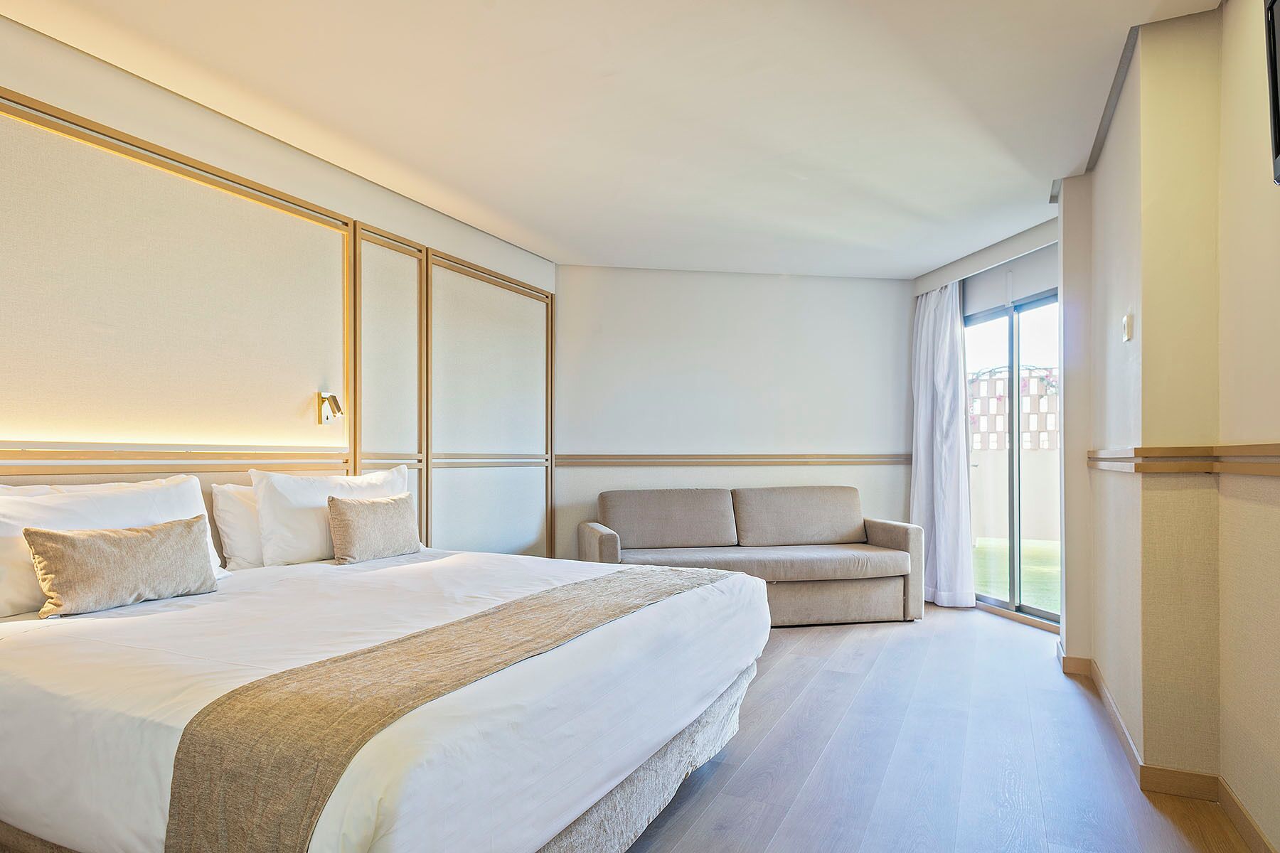 A hotel room with a large bed, a sofa, a large window, and a view of the outdoors.