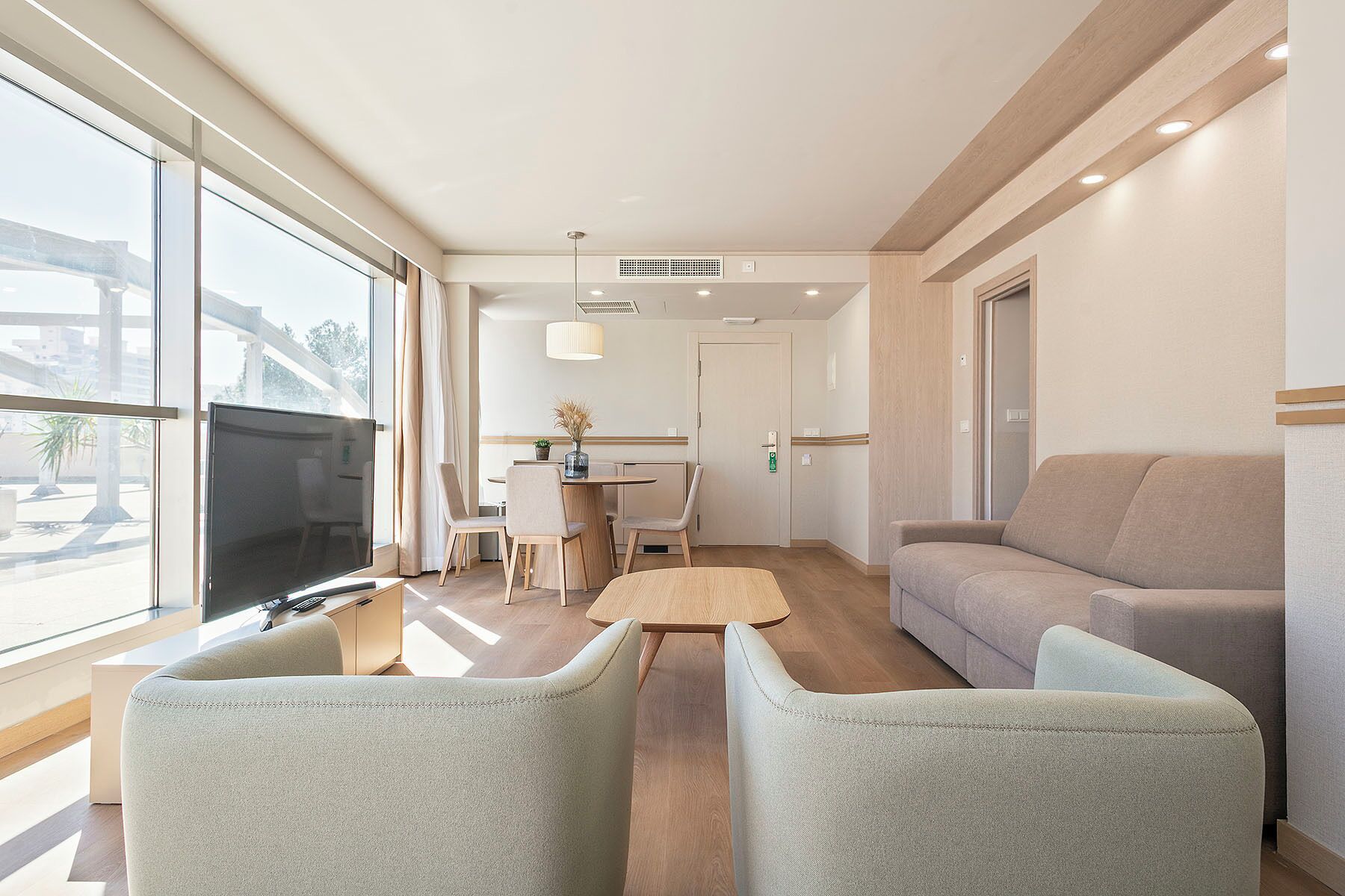 A modern living room with a sofa, two armchairs, a dining area with a table and chairs, and a TV.