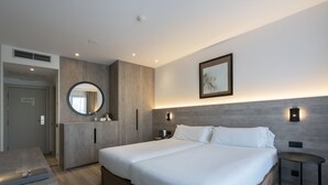 Une chambre d’hôtel moderne avec un grand lit, une table de chevet, un miroir et un luminaire fixé au mur.