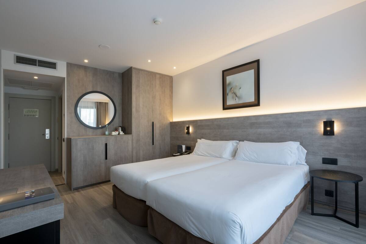 Une chambre d’hôtel moderne avec un grand lit, une table de chevet, un miroir et un luminaire fixé au mur.