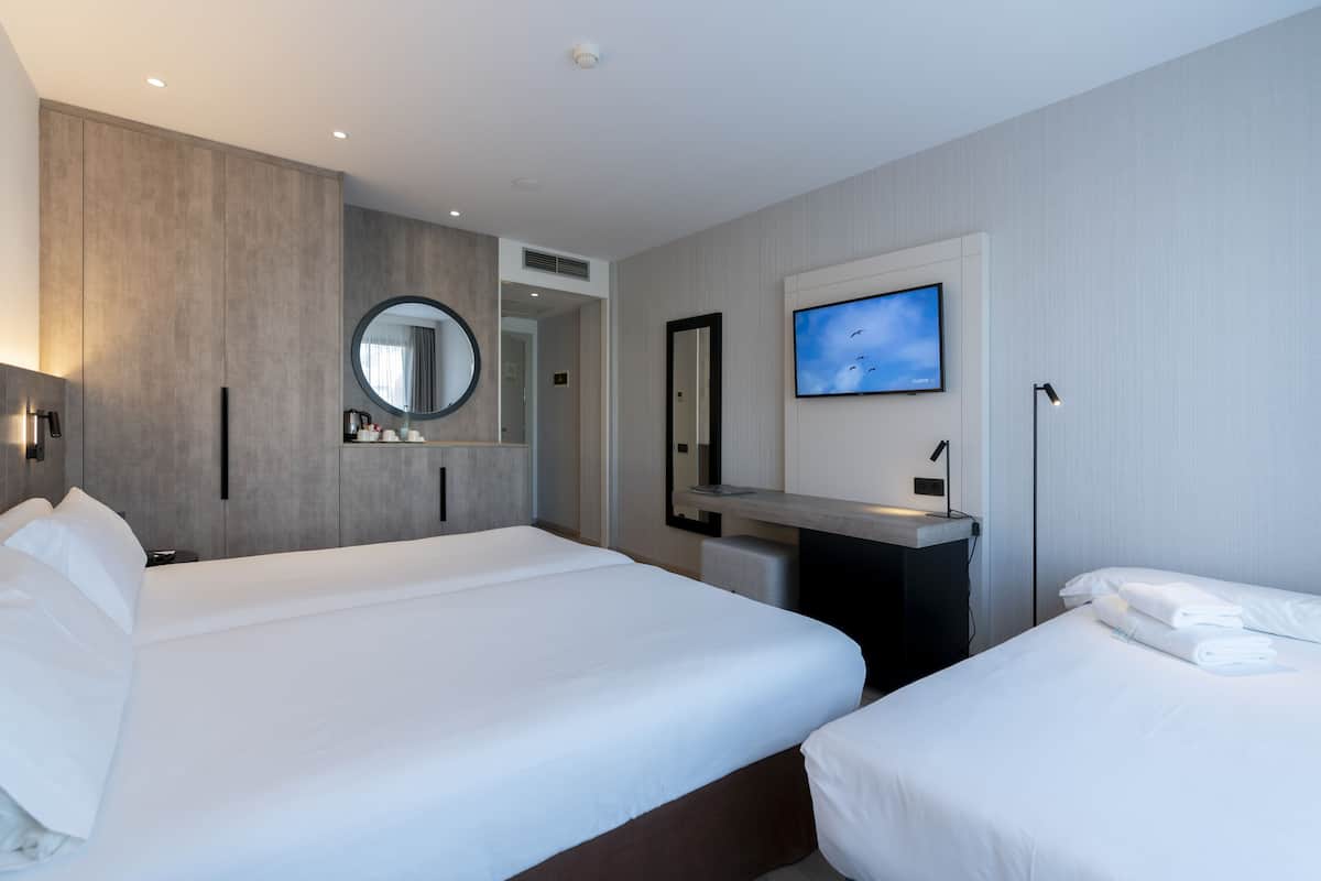 Une chambre d’hôtel moderne équipée de deux lits, d’une télévision, d’un bureau et d’un grand miroir.