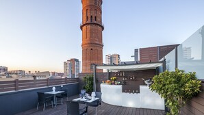 Une terrasse sur le toit avec un espace bar, des sièges et une vue sur une haute tour.