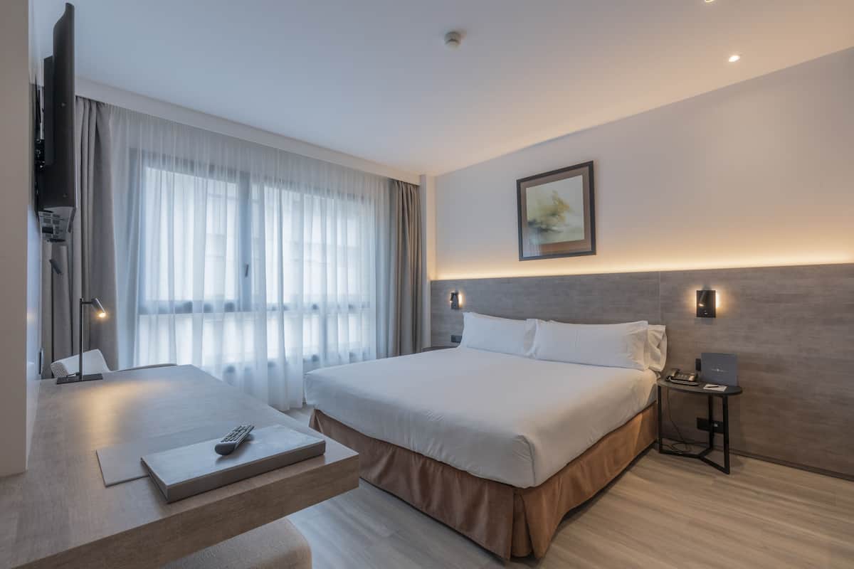 Une chambre d’hôtel moderne dotée d’un grand lit, d’un bureau avec un ordinateur portable et d’une télévision à écran plat.
