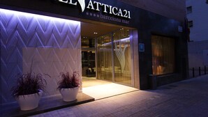 L’extérieur de l’hôtel Attica21 se caractérise par une façade moderne, une grande entrée vitrée et deux plantes en pot placées devant.