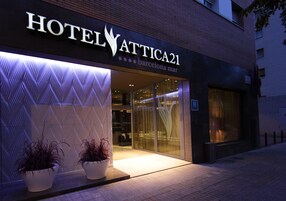 Hotelli Attica21:n ulkoasu on moderni: siinä on suuri lasinen sisäänkäynti ja kaksi ruukussa olevaa kasvia sen edessä.