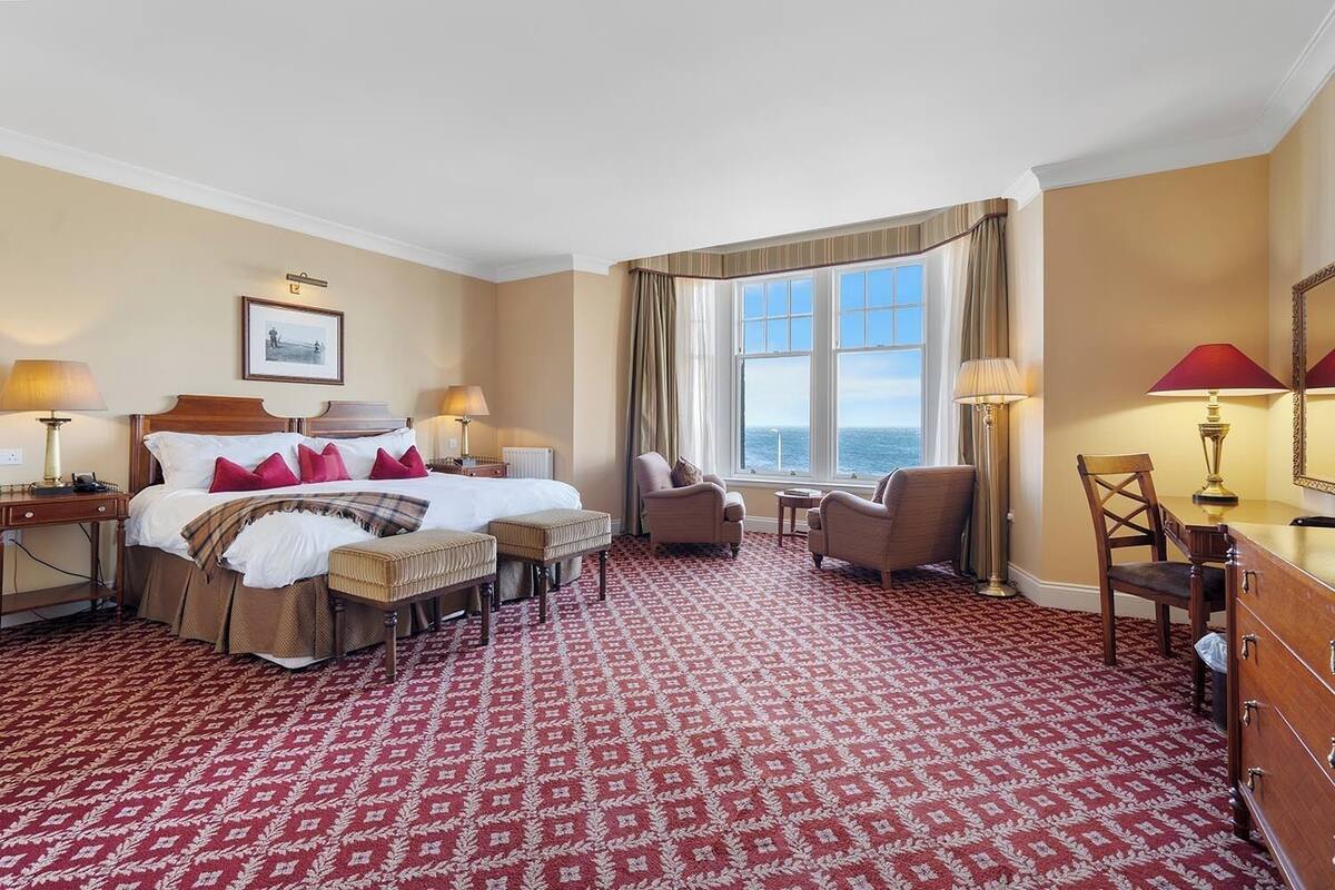 Habitación de hotel con una cama grande, dos sillones, un escritorio y vistas al mar.