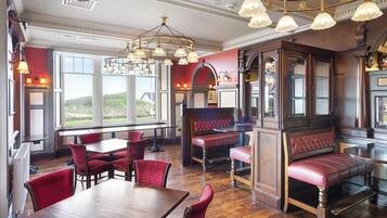 A restaurant with wooden tables and red upholstered booths, large windows, and ornate chandeliers.