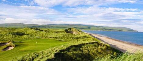 Un campo de golf costero con playa arenosa y dunas cubiertas de césped.