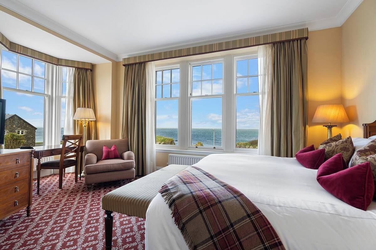 Habitación de hotel con una cama grande, un escritorio, una silla y vista al mar.