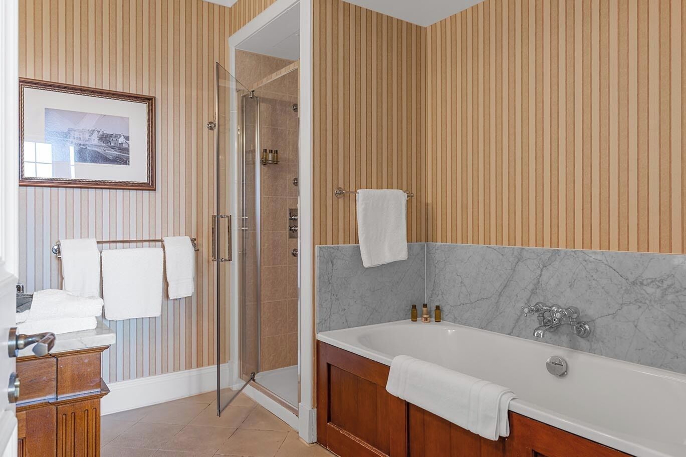 Un baño moderno con cabina de ducha de vidrio, una bañera de mármol y paneles de madera en las paredes.