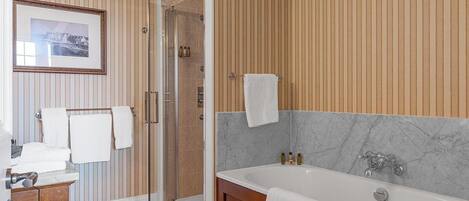 Un baño moderno con cabina de ducha de vidrio, una bañera de mármol y paneles de madera en las paredes.