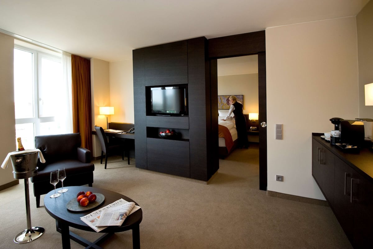 Une chambre d’hôtel équipée d’une télévision à écran plat, d’un coin repas avec une table et des chaises, d’un canapé et d’un mini-bar.