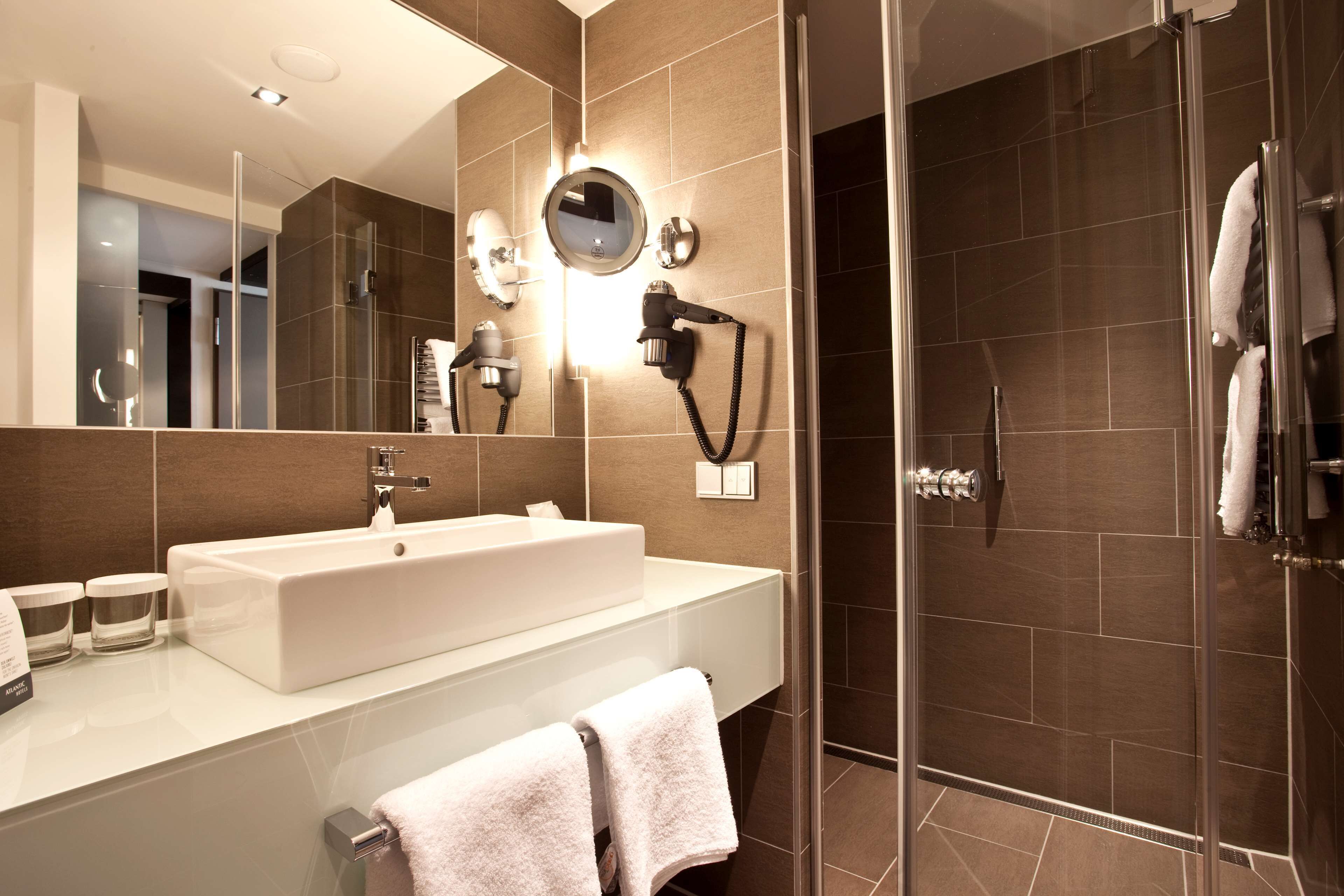 A modern bathroom with a large sink, a mirror, a hairdryer, and a glass-enclosed shower.