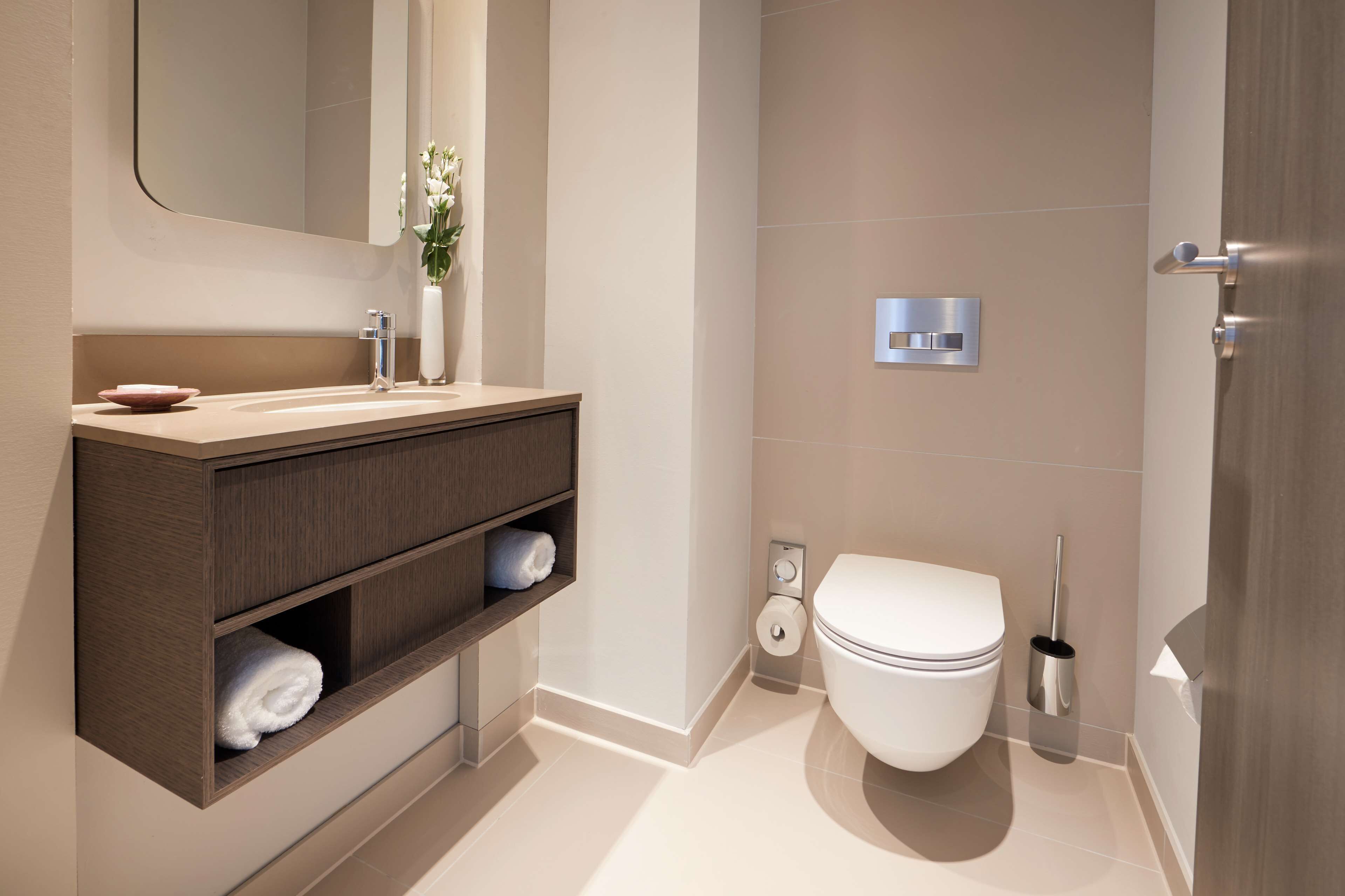Ein modernes Badezimmer mit einem Holzlagerfläschchen, einer weißen Toilette und einem wandmontierten Spülhebel.
