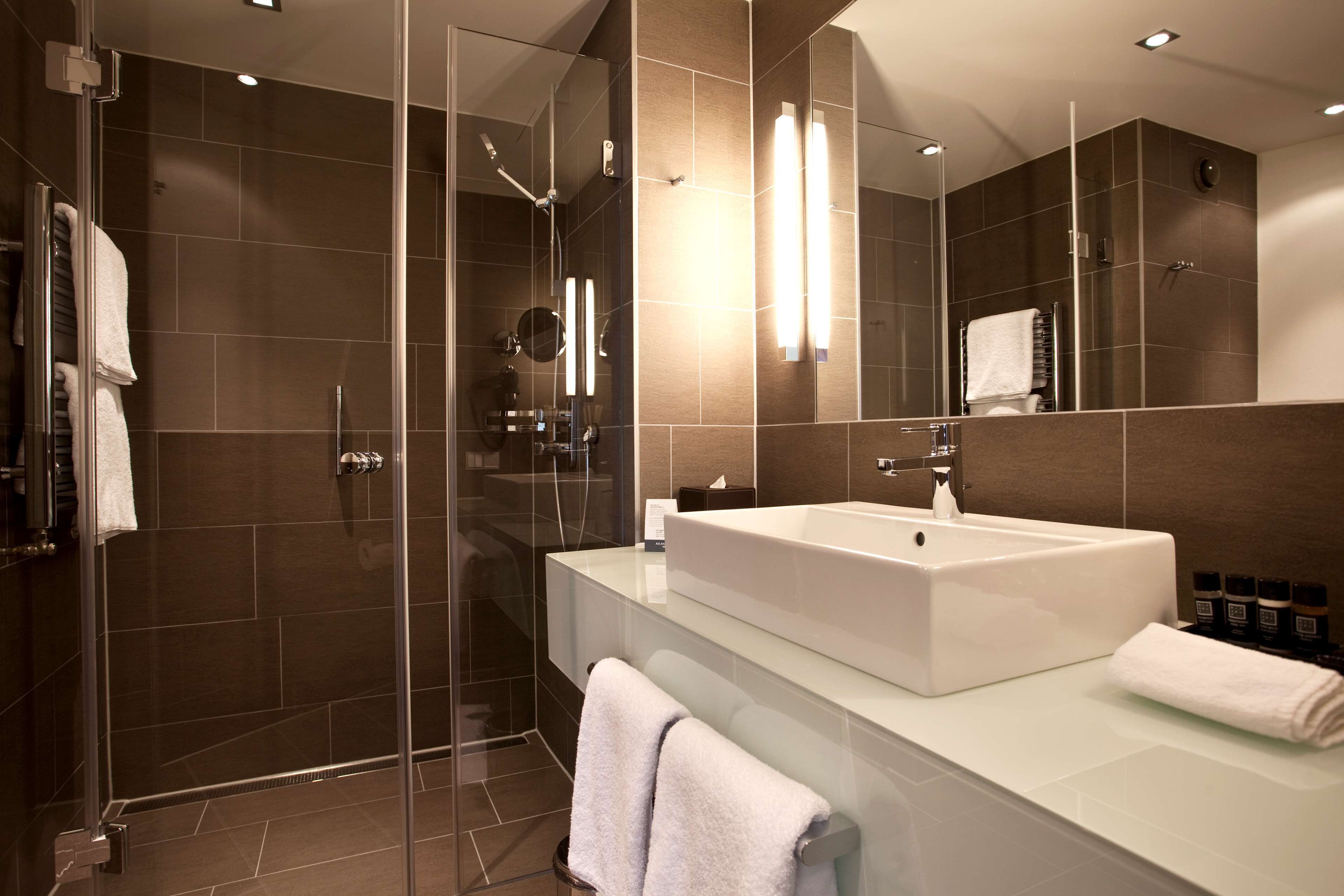 Un bany modern amb plat de dutxa envoltat de vidre, un lavabo gran de color blanc i un mirall amb il·luminació integrada.