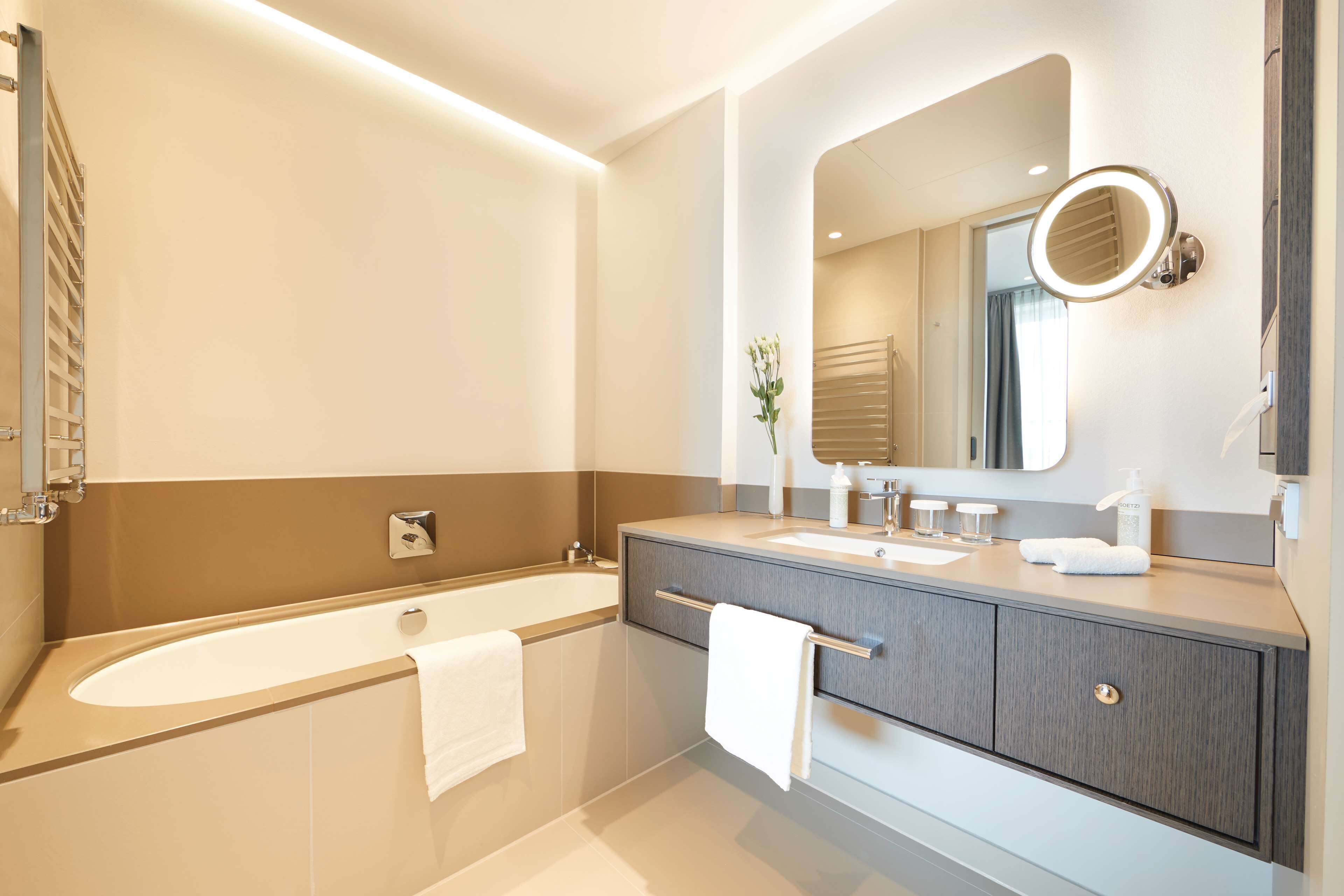 Un baño moderno con bañera, tocador y un espejo grande con luz integrada.
