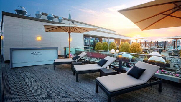 A rooftop lounge area with sun loungers, umbrellas, and a view of the cityscape.