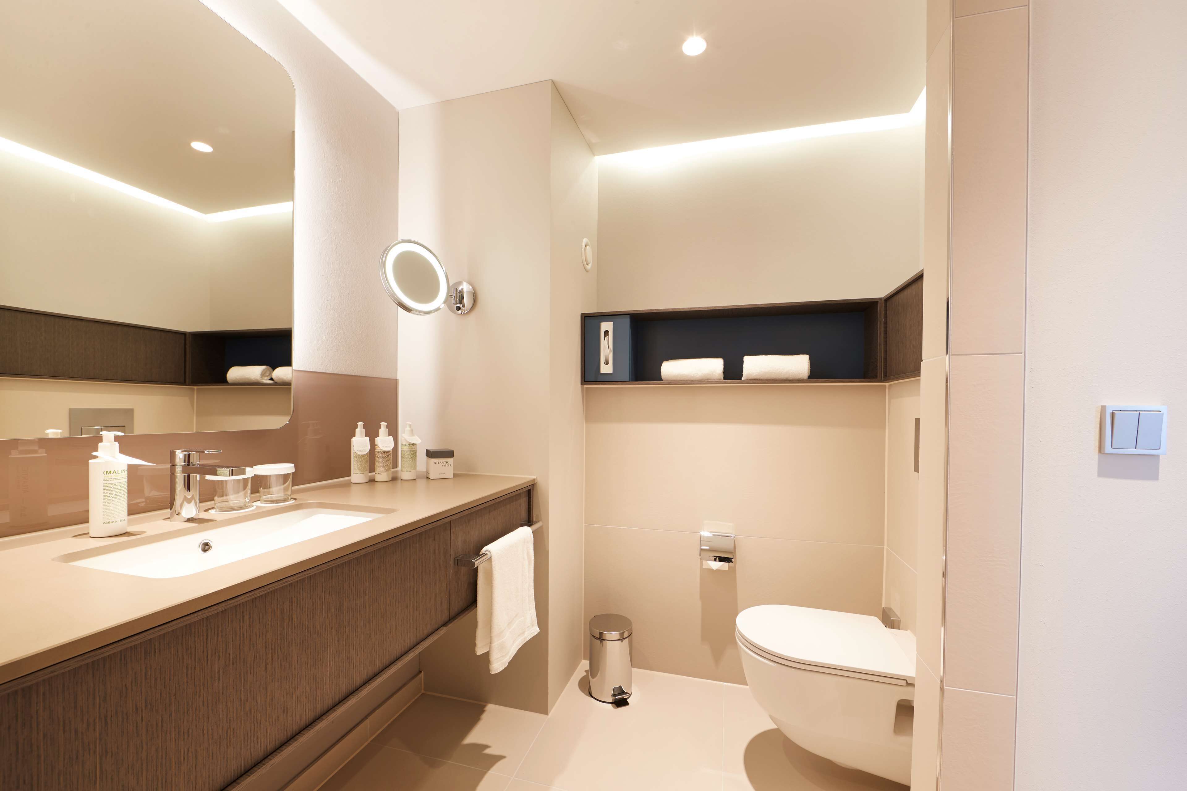Un baño moderno con dos lavamanos, un inodoro y un tocador con espejo.
