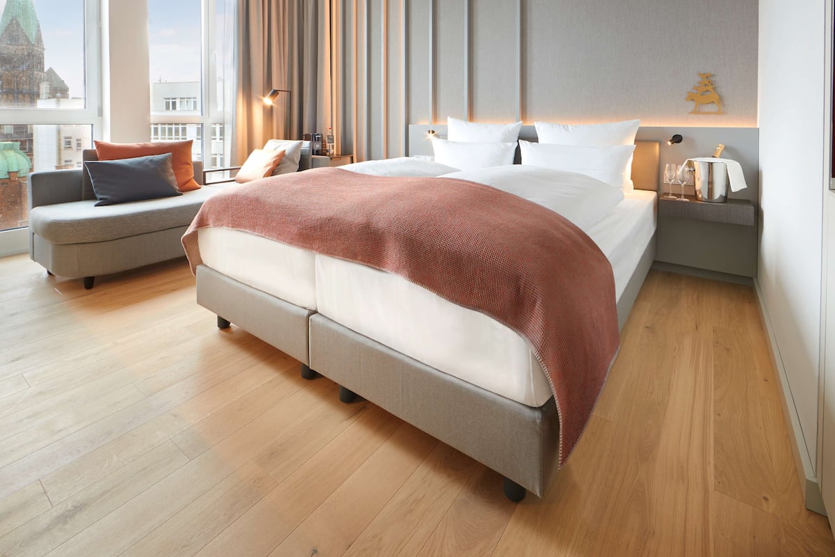 Une chambre d’hôtel moderne avec un grand lit, un canapé et une table de chevet dotée d’une lampe et de quelques verres.