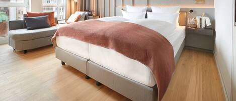 A modern hotel room with a large bed, a sofa, and a nightstand with a lamp and glassware.