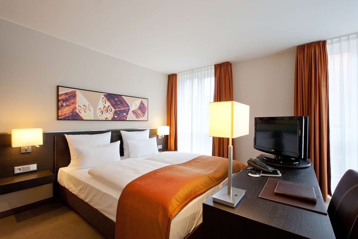 Une chambre d’hôtel avec un lit, un bureau avec un ordinateur, une télévision et une lampe.