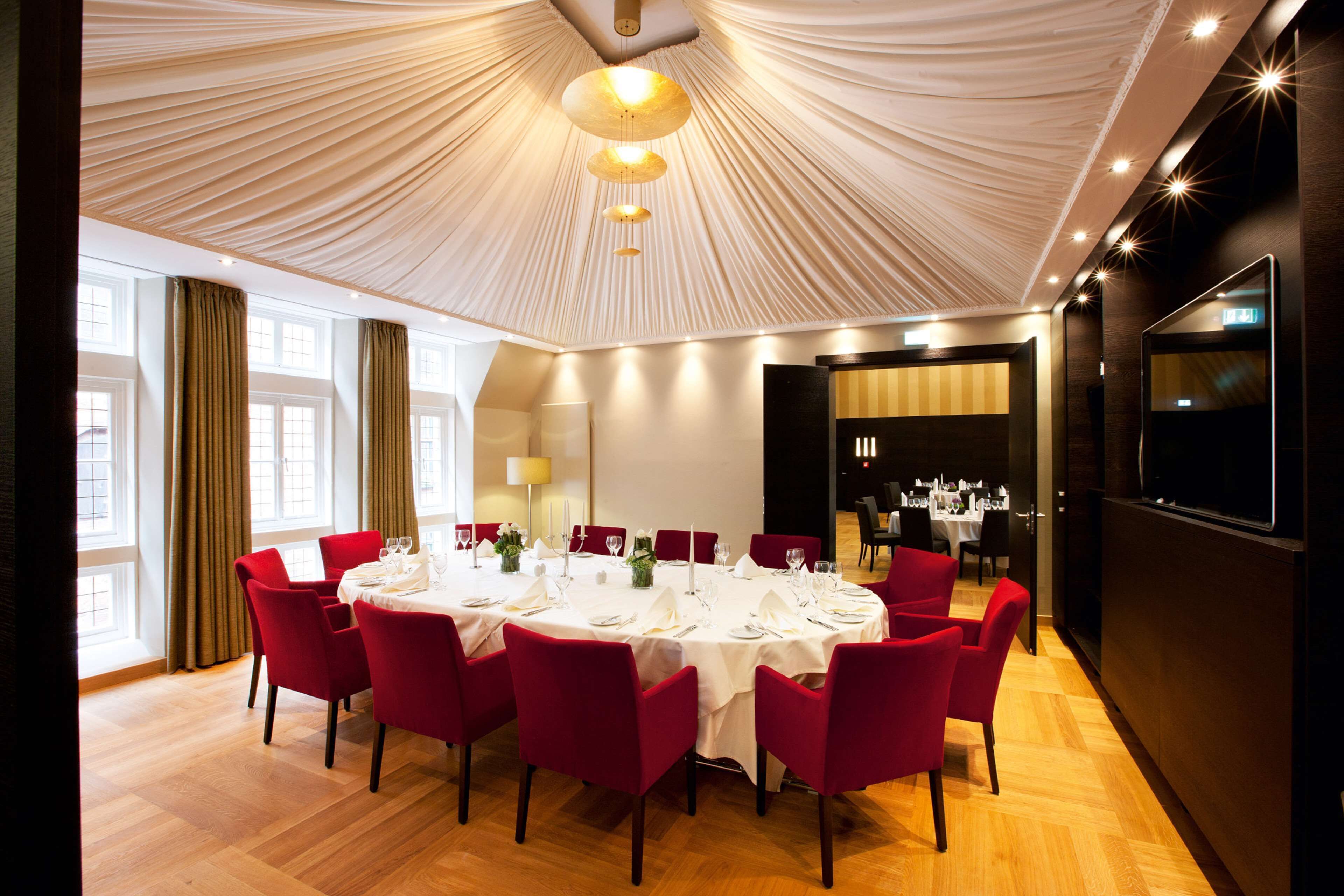 Comedor con una mesa redonda dispuesta para seis personas, rodeada de sillas rojas, bajo un techo cubierto.