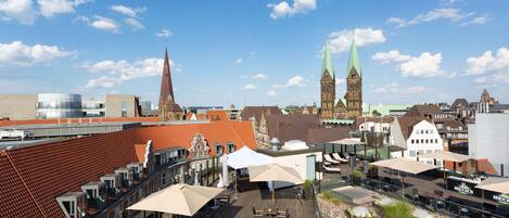 A rooftop terrace with outdoor seating, a view of historic buildings, and a church spire.