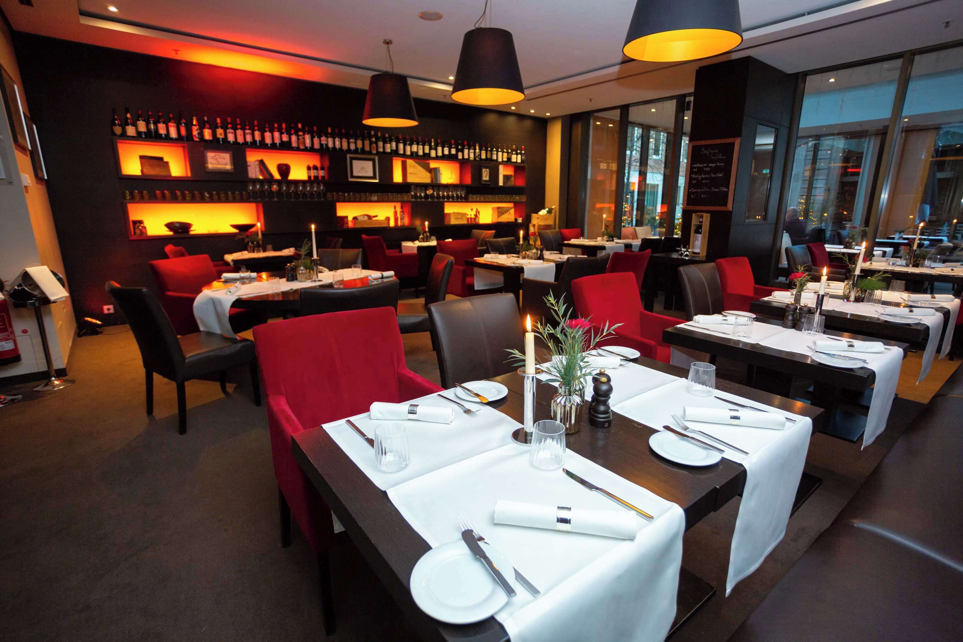 A restaurant with multiple tables set for dining, a bar area with shelves of bottles, and a modern interior design.