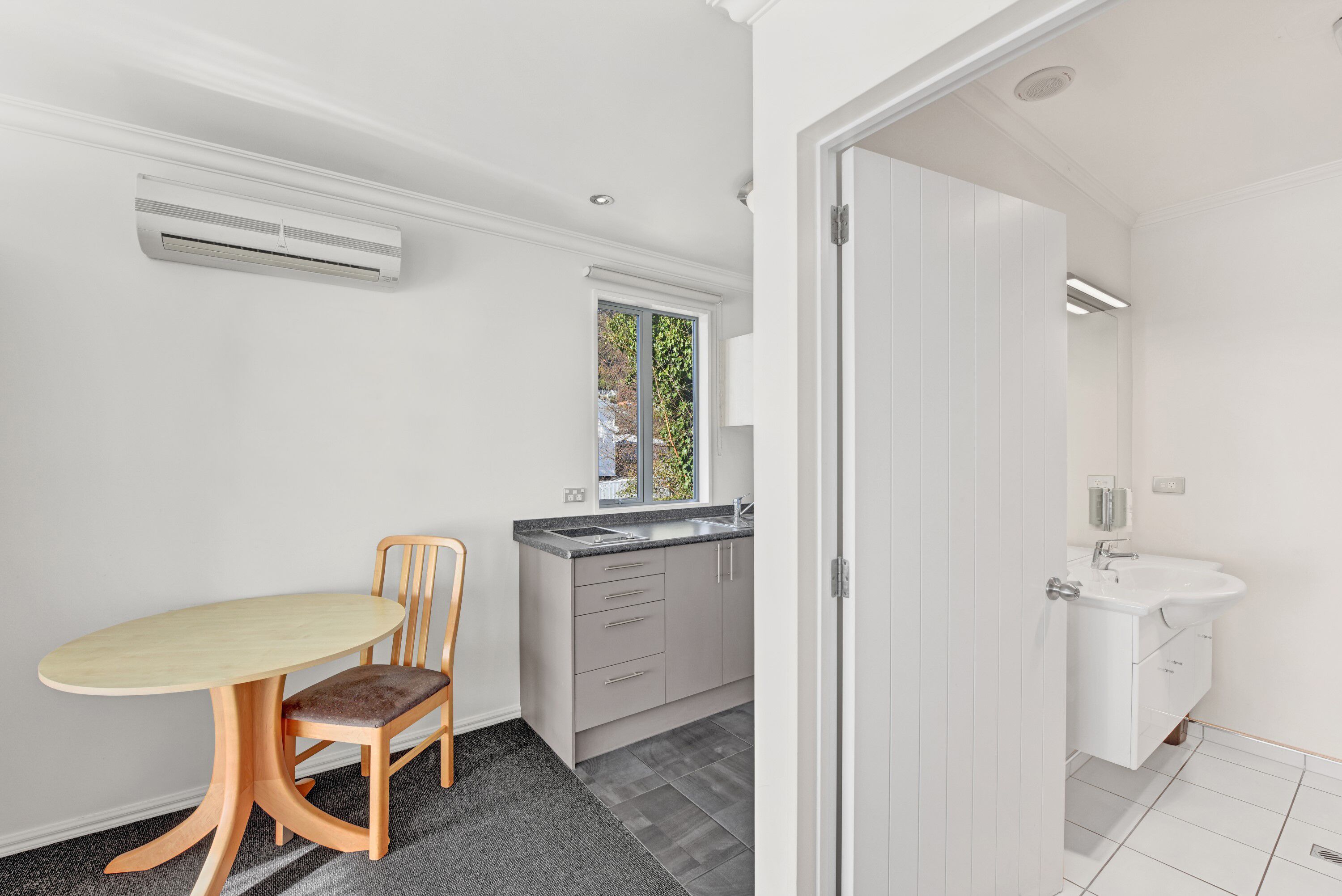 A modern kitchen with a dining table and chairs, a window, and a white sink.