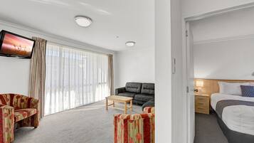 Una habitación de hotel con sofá, una mesita, cama y televisor montado en la pared.
