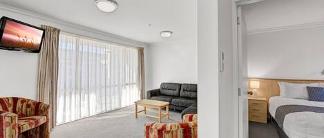 Una habitación de hotel con sofá, una mesita, cama y televisor montado en la pared.