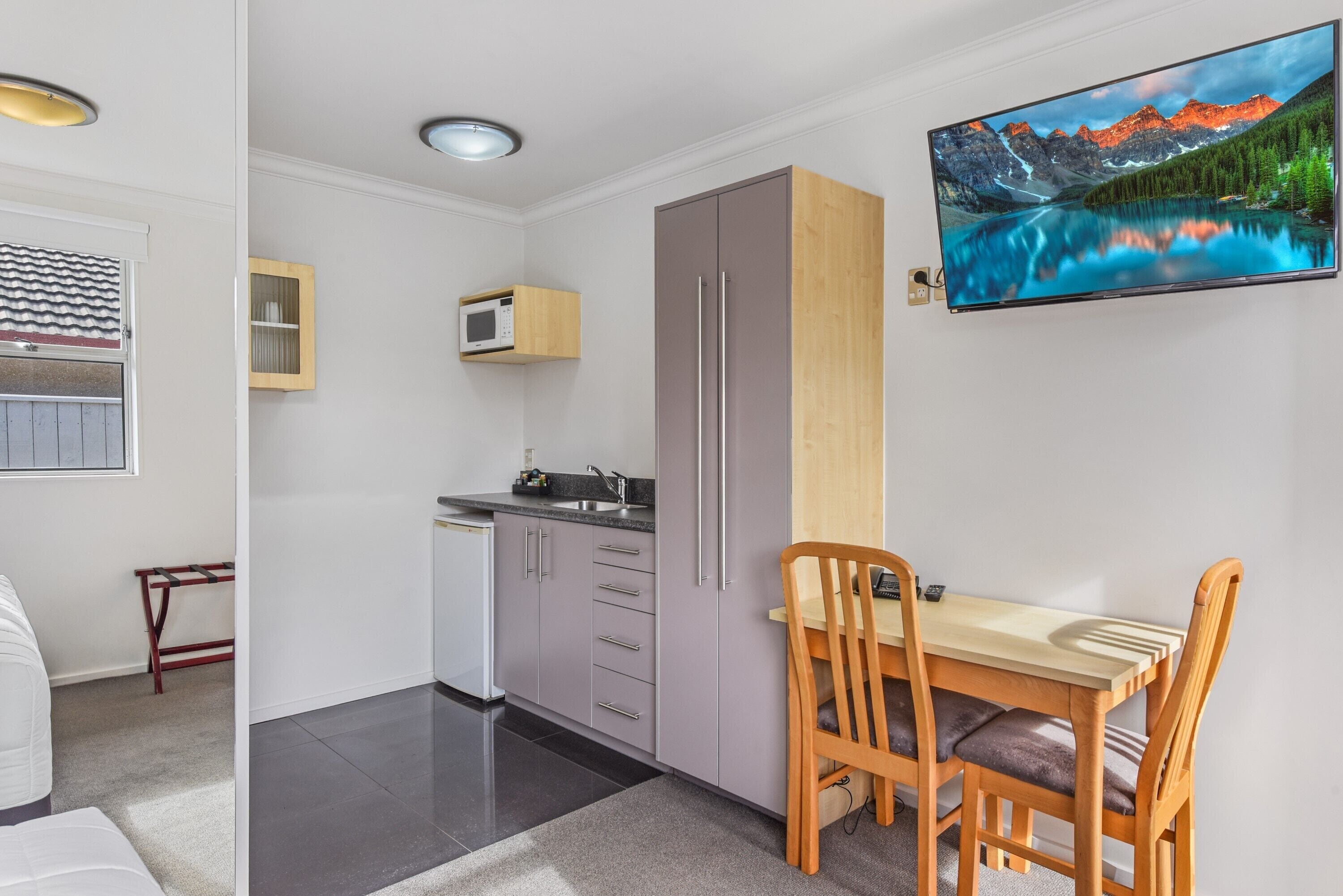 A compact kitchen with grey cabinets, a microwave, and a wooden dining table with chairs.