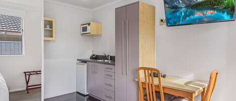 Una cocina compacta con armarios grises, un microondas y una mesa de comedor de madera con sillas.