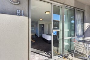 A hotel room with a sliding glass door, a bed, a small table, and a wheelchair-accessible sign. - The Hotel Nelson (Nelson)