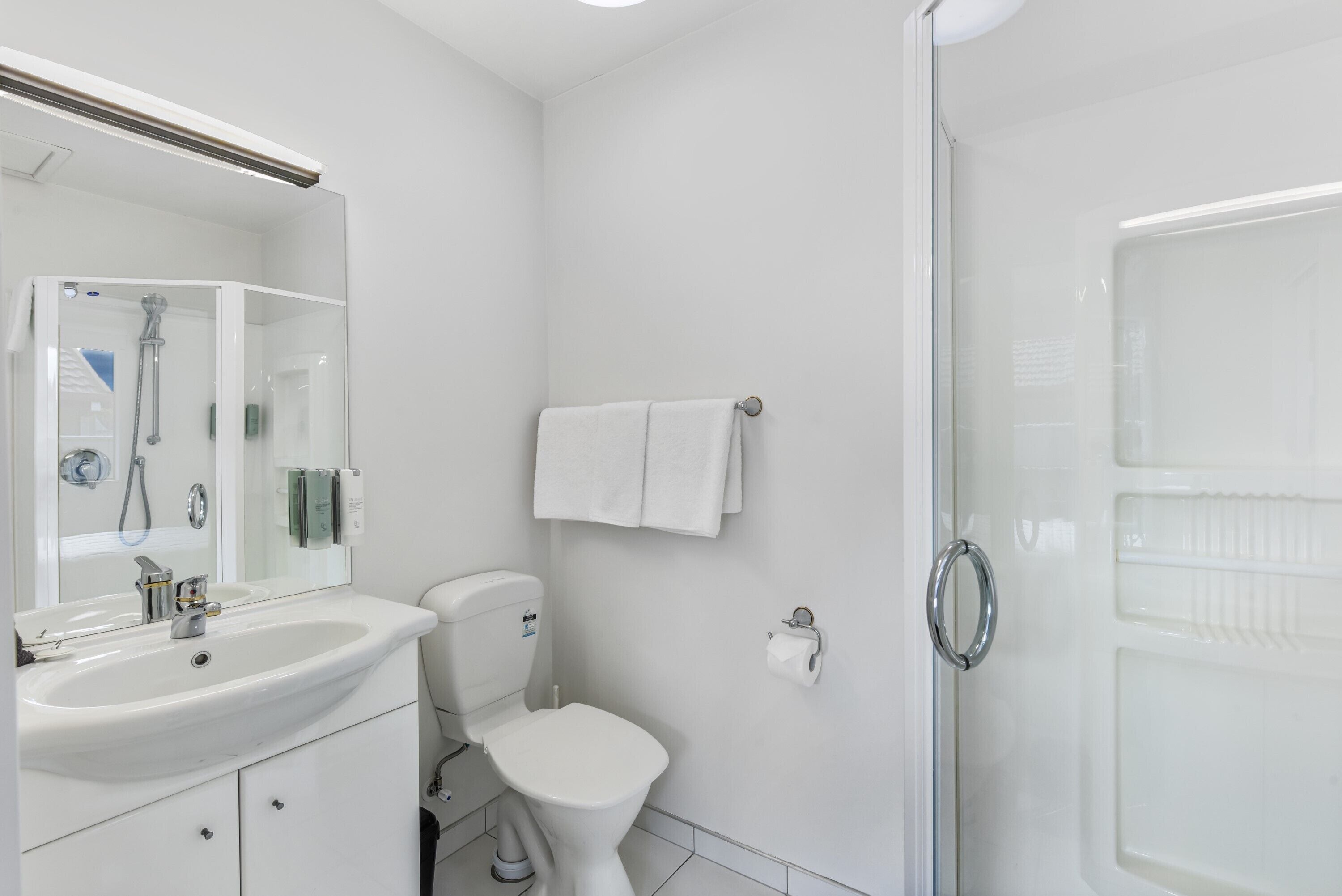 Une salle de bain moderne avec un lavabo, des toilettes et une douche, le tout de couleur blanche.