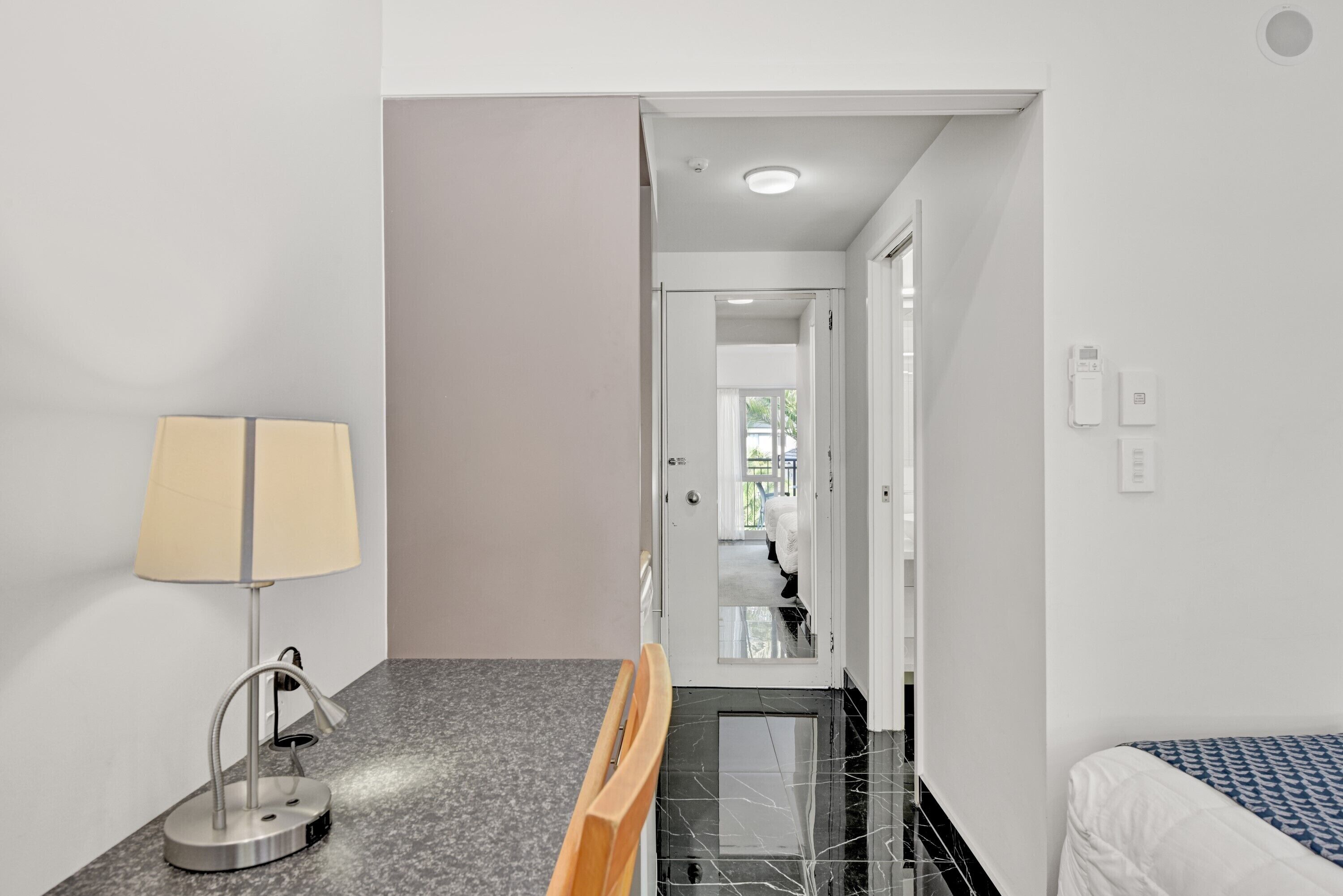 Une chambre d’hôtel avec un lit, un bureau doté d’une lampe, une chaise et une salle de bain visible à travers une porte ouverte.